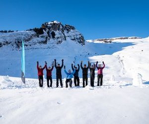 Group of people in the snow, raising arms, mountains in the background, blue flag on the left, winter clothing.