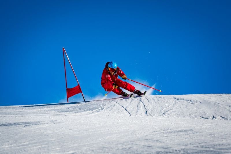 Skifahrer in roter Kleidung mit Helm fährt auf schneebedecktem Hang neben roten Torstangen.