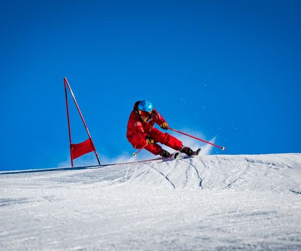 Skier in red clothing with a helmet is skiing on a snow-covered slope next to red gate poles.