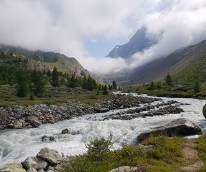 Mountain stream flowing through a rocky valley with green vegetation and misty peaks in the background.