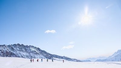 Personengruppe mit Winterkleidung wandert über schneebedeckte Berge unter klarem Himmel.