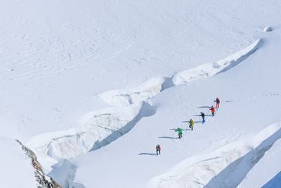 Gruppe von Bergsteigern mit Helmen und Seilen überquert schneebedeckten Gletscher in den Alpen.