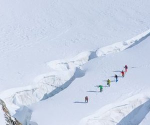 Group of mountaineers with helmets and ropes crossing a snow-covered glacier in the Alps.