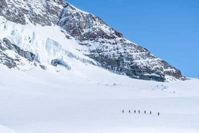 Personengruppe mit Winterkleidung wandert im Schnee vor einer verschneiten Bergkulisse.