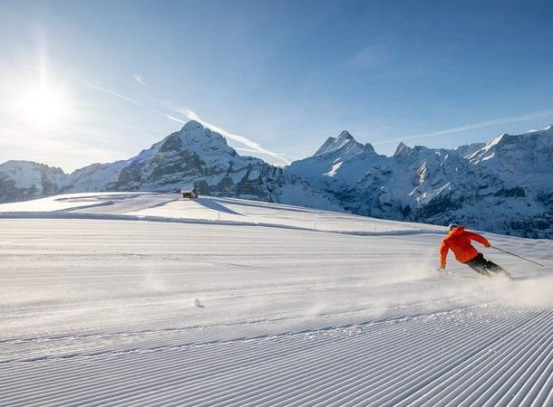 Person auf Skiern fährt eine präparierte Piste hinunter, umgeben von schneebedeckten Bergen.