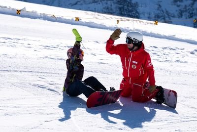 Zwei Personen in Snowboardausrüstung geben sich auf einem verschneiten Berghang ein High-Five, tragen Helme und Schutzbrillen.