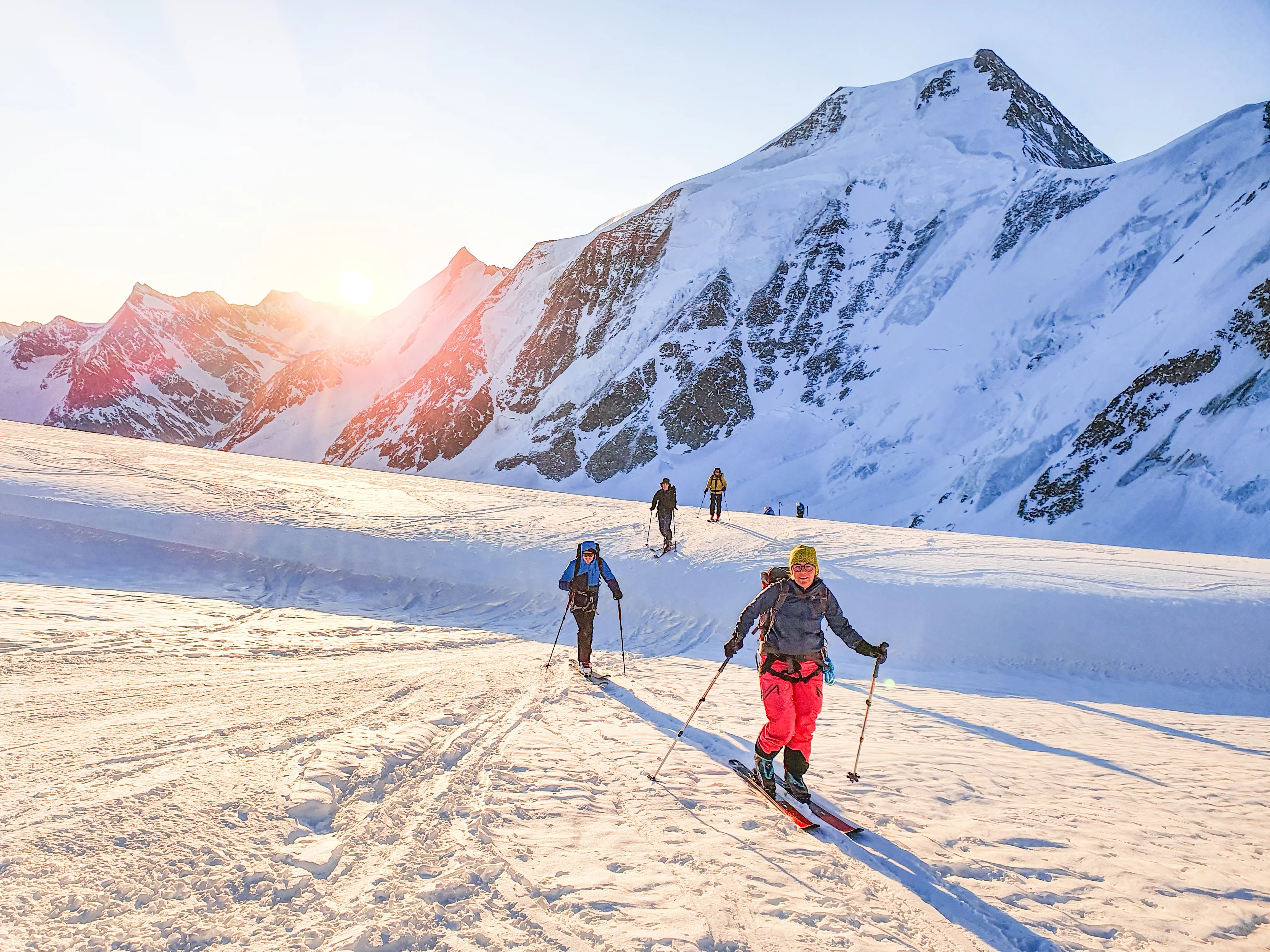 Skitourengänger im Aufstieg mit Sonnenaufgang im Hintergrund