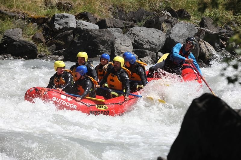 Gruppe beim Wildwasser-Rafting in einem roten Schlauchboot, mit Helmen und Schwimmwesten auf einem Fluss.