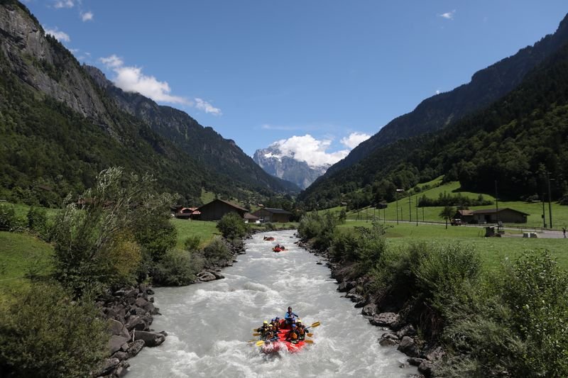 Personen in einem Schlauchboot beim Rafting auf einem Fluss in einem alpinen Tal mit Bergen.