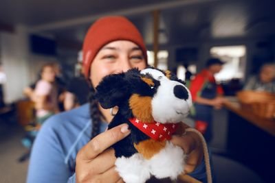 Person holding a stuffed animal in a hut, wearing a red hat. Background blurred.