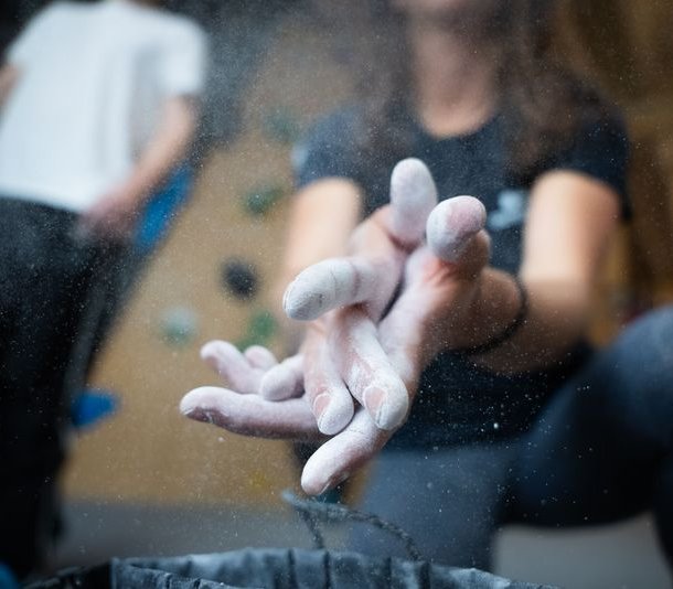 Climber applying chalk to hands in an indoor climbing gym, blurred wall holds in background.