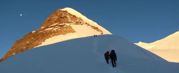 Climbers with backpacks and ropes ascend a snowy mountain slope under a clear blue sky.