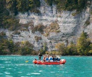 People in an inflatable boat on a turquoise lake, surrounded by rocks and trees.