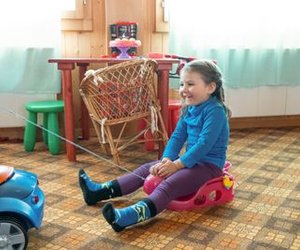 A child is sitting on a toy car in the room while being pulled by another toy car.