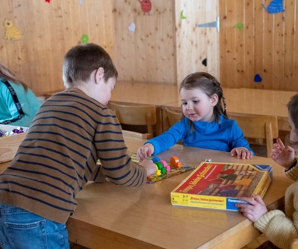 Children are playing with building blocks at a wooden table in a room with wooden walls.