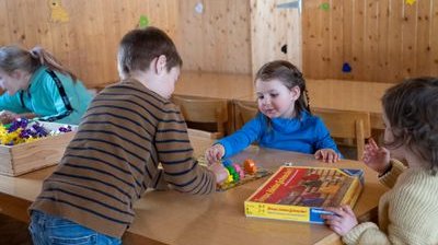 Children are playing with building blocks at a wooden table in a room with wooden walls.