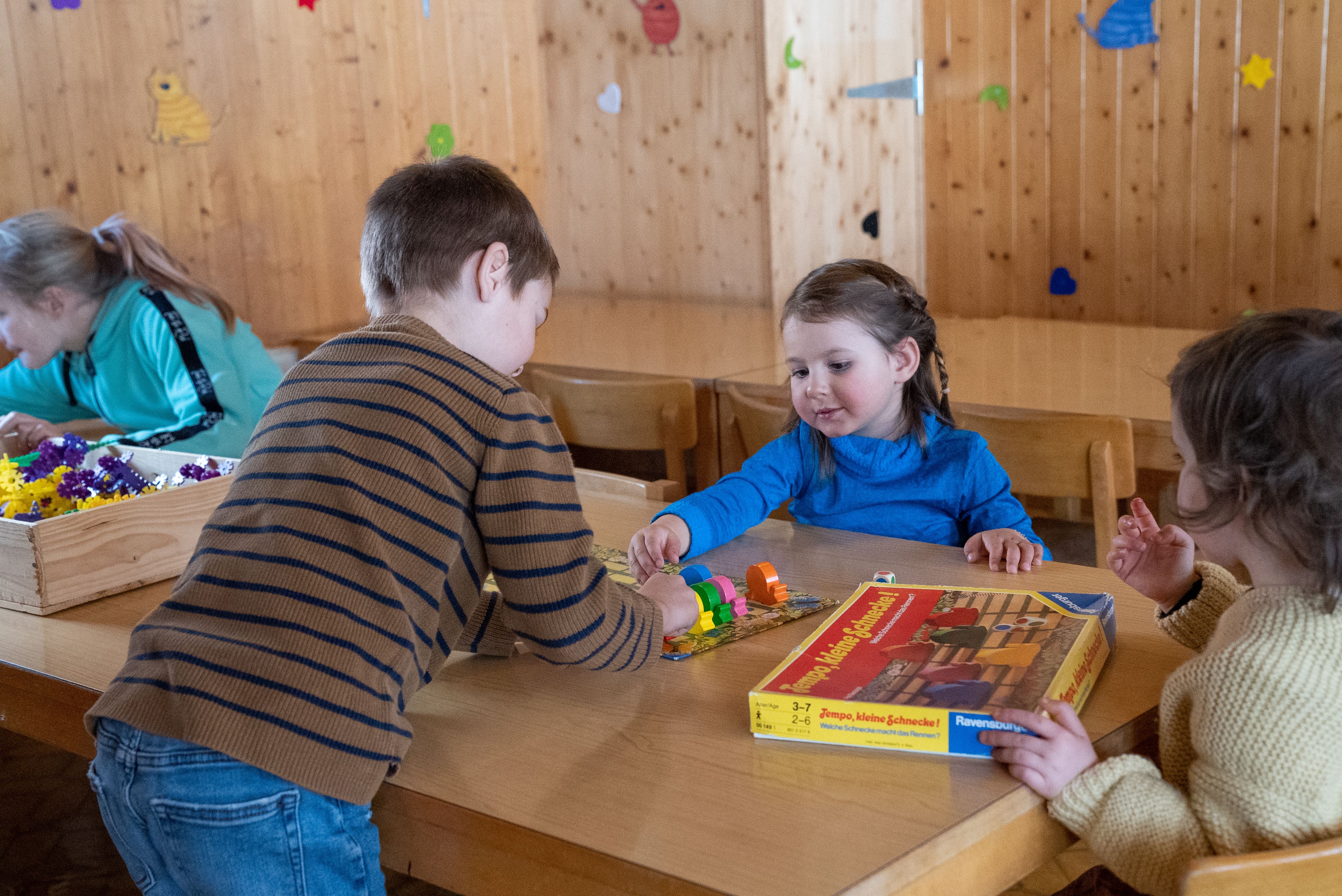 Children are playing with building blocks at a wooden table in a room with wooden walls.