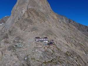 Mountain hut on a rocky slope with a glacier in the background under a clear blue sky.