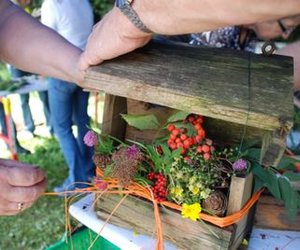 People are decorating a wooden birdhouse with colorful flowers and berries on a table outdoors.