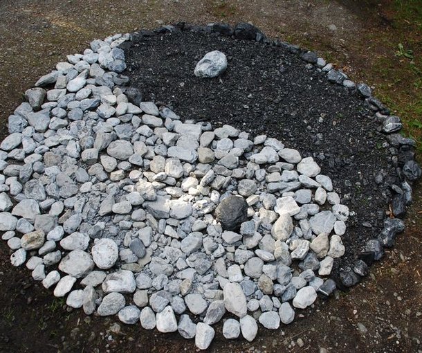 Stone pattern in the shape of a Yin-Yang symbol on the ground, surrounded by grass.