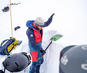 Mountain guide shows avalanche course participants snow structure with avalanche shovel.