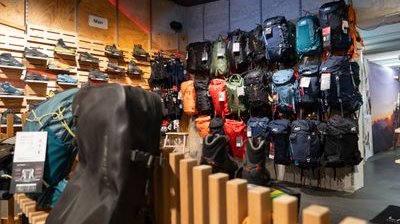 Rucksäcke und Wanderschuhe in einem Outdoor-Geschäft, auf Regalen und an Wänden ausgestellt.