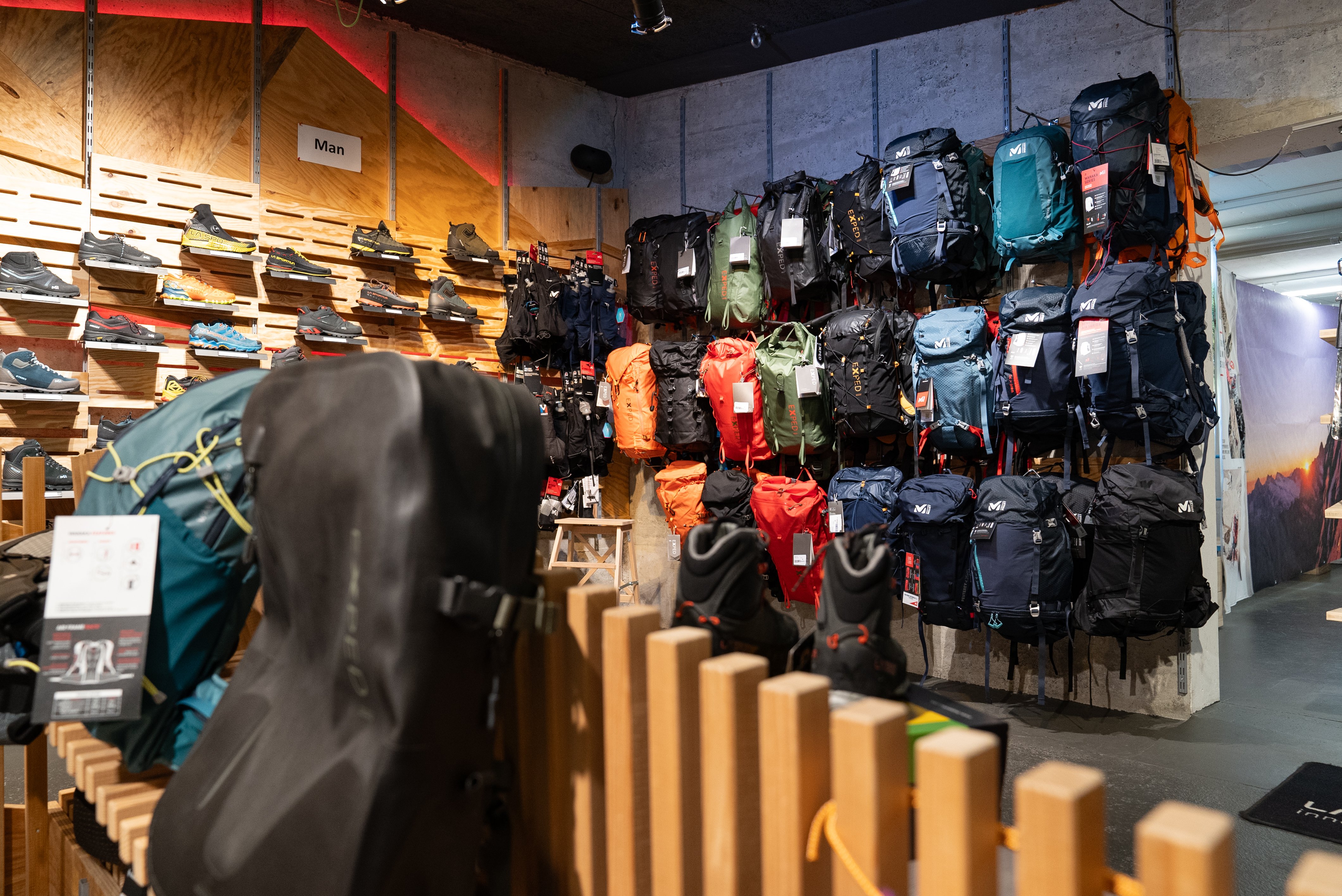 Rucksäcke und Wanderschuhe in einem Outdoor-Geschäft, auf Regalen und an Wänden ausgestellt.