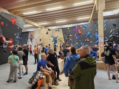 벽에는 다양한 색상의 홀드가 있고 일부 사람들은 클라이밍화를 신고 있는 실내 클라이밍 체육관에 있습니다.