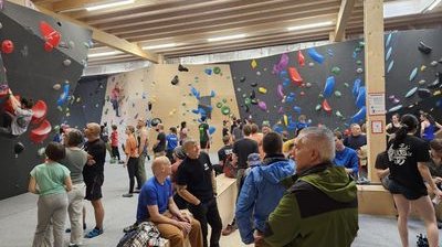 벽에는 다양한 색상의 홀드가 있고 일부 사람들은 클라이밍화를 신고 있는 실내 클라이밍 체육관에 있습니다.