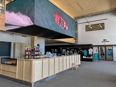 목재로 된 카운터가 있는 리셉션 영역, 위에 디지털 스크린, 그리고 진열된 상품들이 있습니다.