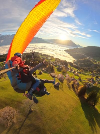 Zwei Personen beim Gleitschirmfliegen über einer grünen Landschaft, mit Helmen und Gurtzeug.