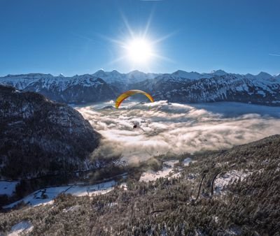 Gleitschirmflieger mit Helm über verschneiten Bergen und Wolken in der Schweiz.