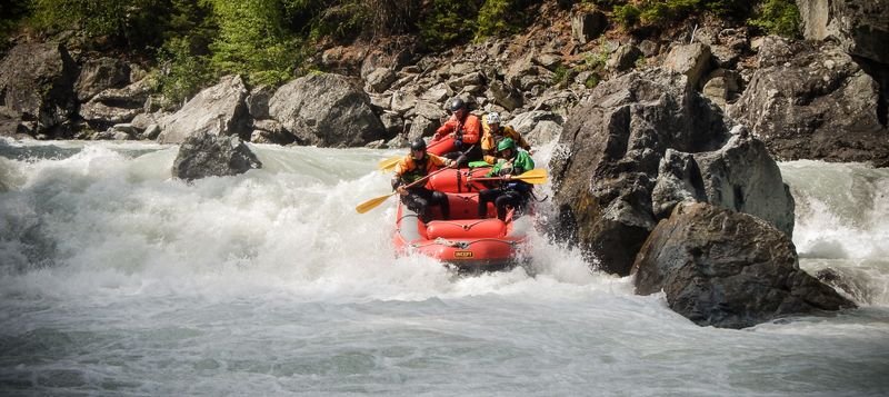 People in an inflatable boat doing whitewater rafting, wearing helmets and life jackets, rocks.