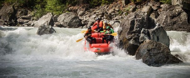 People in an inflatable boat doing whitewater rafting, wearing helmets and life jackets, rocks.