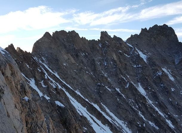 Jagged mountain peaks with patches of snow under a partly cloudy sky.