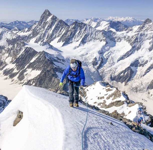 Climber ascends snowy mountain ridge, surrounded by peaks.