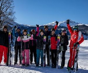 Group of skiers in helmets and goggles, holding skis on snowy mountain slope with clear sky.