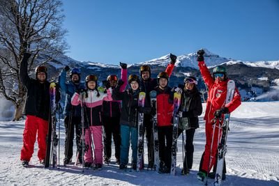 Group of skiers in helmets and goggles, holding skis on snowy mountain slope with clear sky.