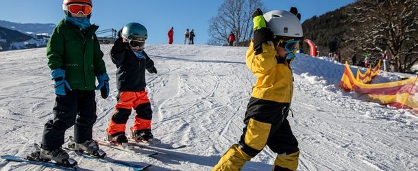 Three children with helmets and skis on a snow-covered slope in the mountains.