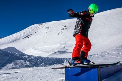 Person auf Snowboard mit grünem Helm auf einer Box im verschneiten Berggebiet.