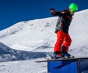 Person on snowboard with green helmet on a box in a snowy mountain area.