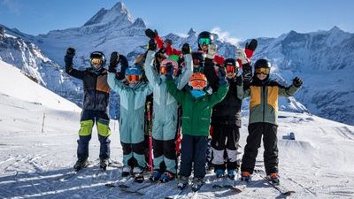 Group of skiers with helmets and ski goggles on a snow-covered mountain in front of an alpine backdrop.