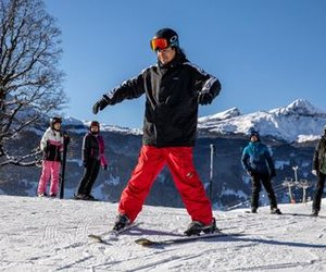 A group of skiers on a snowy mountain slope, wearing helmets and ski gear, with mountains in the background.