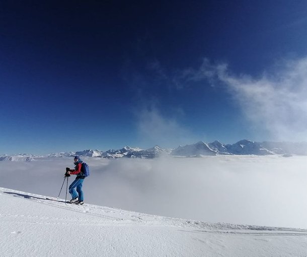 Ski tourers ascending with a sea of fog and mountains in the background