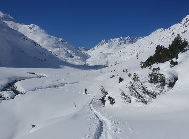 Ski tourers ascending through a snow-covered valley with a stream.