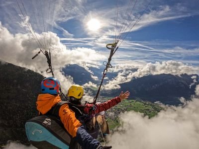 Zwei Personen beim Paragliding über einer Berglandschaft, mit Helmen und Gurten ausgestattet.