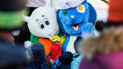 Two people in animal costumes surrounded by children in winter clothing at an outdoor event.