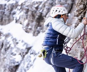 Climber with helmet and rope on a rock face in snow-covered mountains.