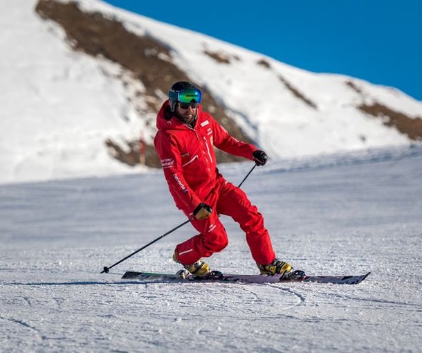 Skier in red suit with helmet and ski goggles on snow-covered mountain.