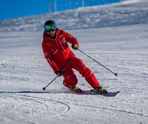 Skier in a red suit with a helmet and ski goggles skiing downhill on a snowy slope.